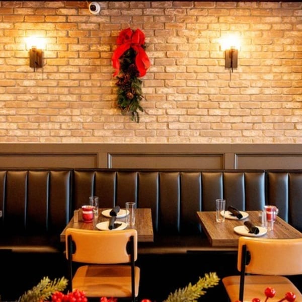 Craft Kitchen + Bar interior with brick wall, sconces, holiday garland, and set tables with booths.