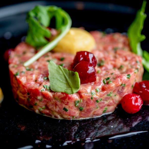Craft Kitchen + Bar's beef tartare, garnished with mustard, cranberries, and fresh greens on a dark plate.