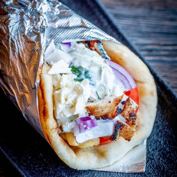 Close-up of a Craft Kitchen + Bar chicken gyro with feta, red onion, and tzatziki sauce.