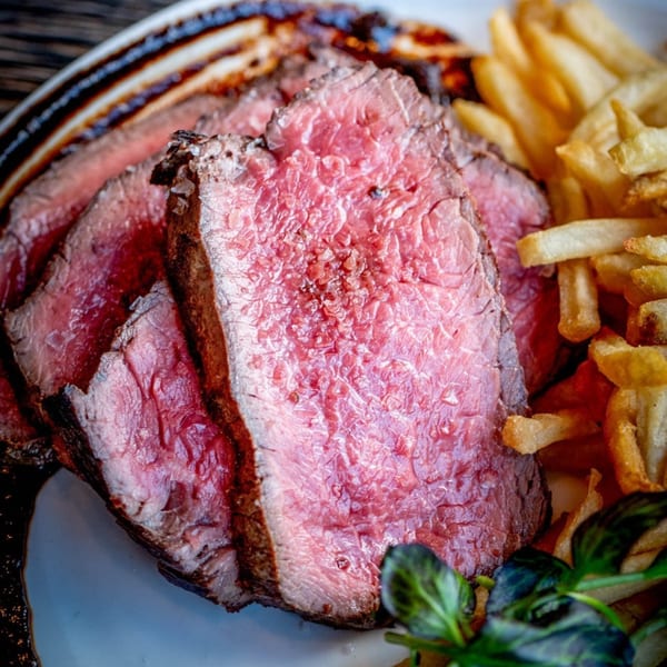 Sliced medium-rare steak with a side of golden french fries and a green garnish on a white plate.