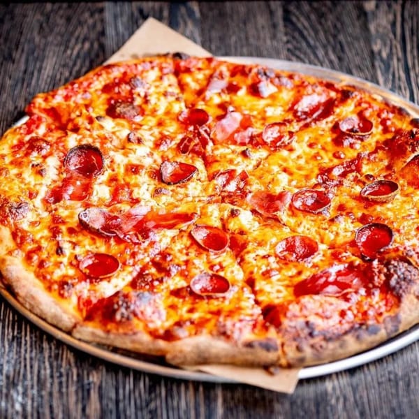 A large, sliced pepperoni pizza with melted cheese on a metal tray, on a dark wooden table.