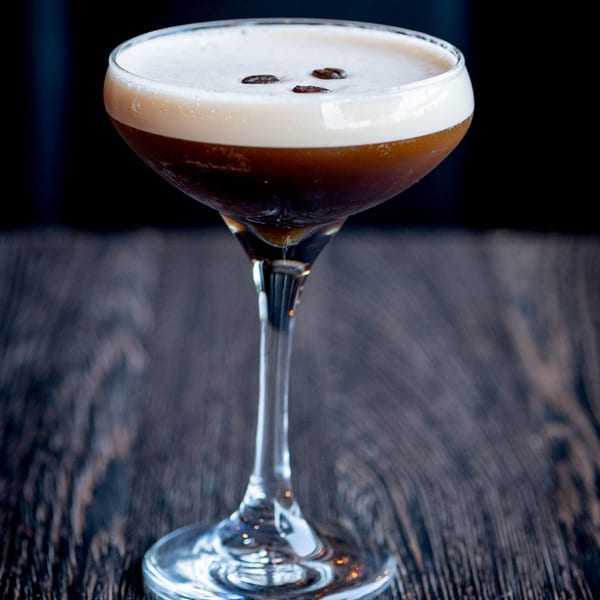 Espresso martini with a foamy top and three coffee beans, on a dark wooden table.