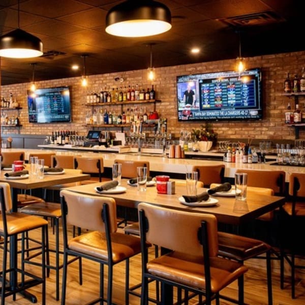 Interior of Craft Kitchen + Bar, featuring a long bar, high-top tables, and TVs showing sports.